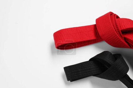 Cinturones de karate rojos y negros sobre fondo blanco, plano. Espacio para texto