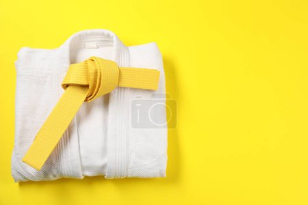 Karate belt and white kimono on yellow background, top view. Space for text