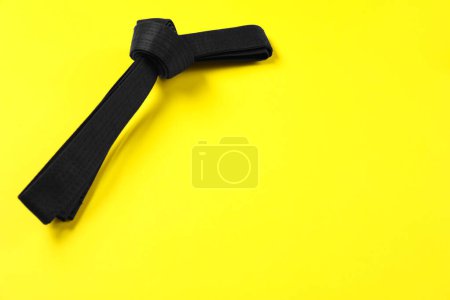 Téléchargez les photos : Ceinture karaté noire sur fond jaune, espace pour le texte - en image libre de droit