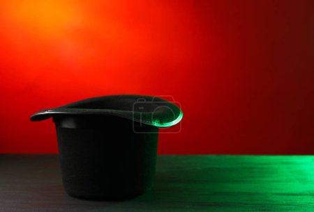 Magician's hat on black wooden table against color background, space for text
