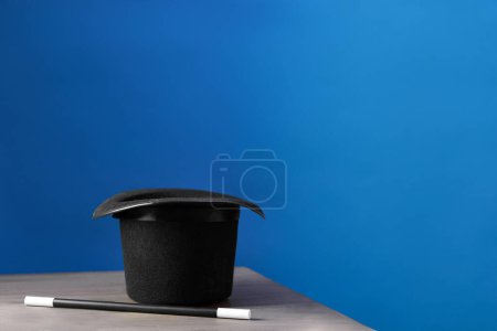 Magician's hat and wand on wooden table against blue background, space for text