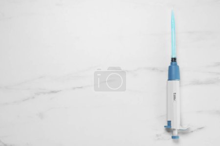 Photo for Laboratory analysis. Micropipette with liquid on white marble table, top view. Space for text - Royalty Free Image