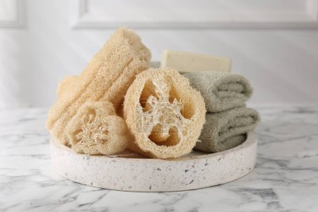Loofah-Schwämme, Handtücher und Seife auf weißem Marmortisch