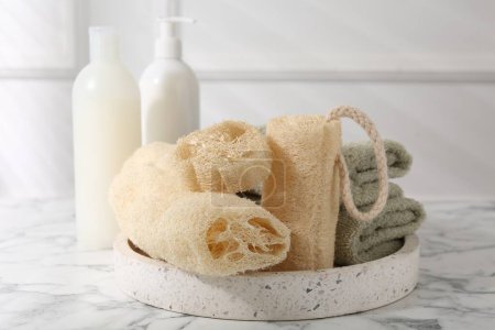 Loofah sponges, towels and cosmetic products on white marble table