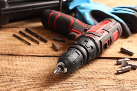 Electric screwdriver with bits and drills on wooden table, closeup