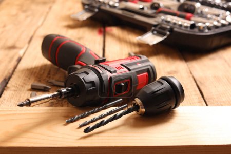 Electric screwdriver with bits and drills on wooden table, closeup