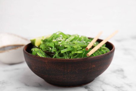 Tasty seaweed salad in bowl served on white marble table, closeup