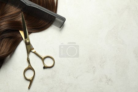 Tijeras de peluquería profesional y peine con hebra de pelo marrón en la mesa gris, vista superior. Espacio para texto