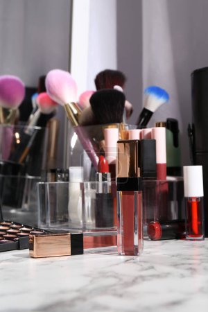 Foto de Brillante brillo labial entre diferentes productos cosméticos en tocador blanco - Imagen libre de derechos