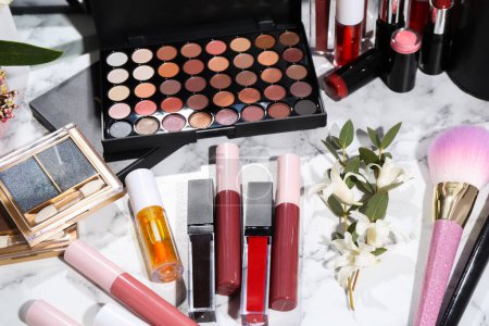 Foto de Brillante brillo labial entre diferentes productos cosméticos en tocador blanco - Imagen libre de derechos