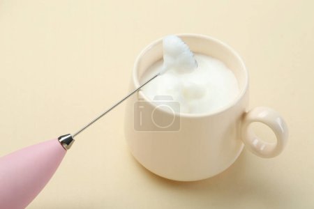 Mini mélangeur (mousseur de lait) et tasse de lait fouetté sur fond beige, gros plan