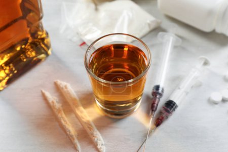 Photo for Alcohol and drug addiction. Whiskey in glass, syringes and cocaine on white table, closeup - Royalty Free Image