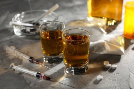 Photo for Alcohol and drug addiction. Whiskey in glasses, syringes, pills and cocaine on grey table - Royalty Free Image
