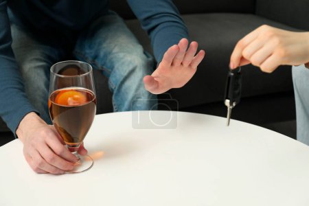 Téléchargez les photos : Homme avec un verre de boisson alcoolisée refusant voiture tandis que la femme lui suggérant des clés, gros plan. Ne pas boire et conduire concept - en image libre de droit