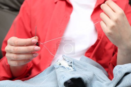 Woman sewing jeans with needle, closeup view