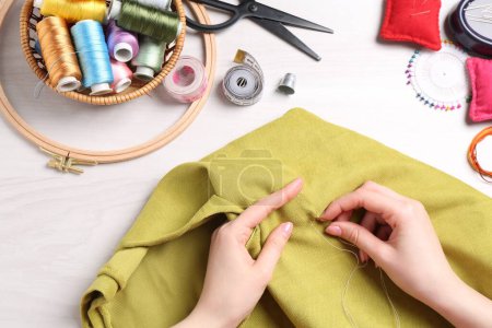 Woman with sewing thread embroidering on cloth at white wooden table, top view