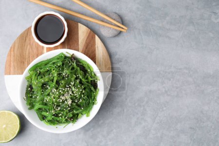 Tasty seaweed salad in bowl served on gray table, flat lay. Space for text