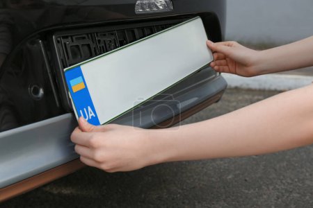Mujer instalando placa de matrícula del vehículo al aire libre, primer plano