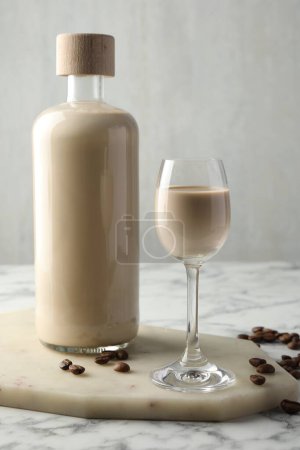 Téléchargez les photos : Liqueur de crème de café en verre, haricots et bouteille sur table en marbre blanc - en image libre de droit