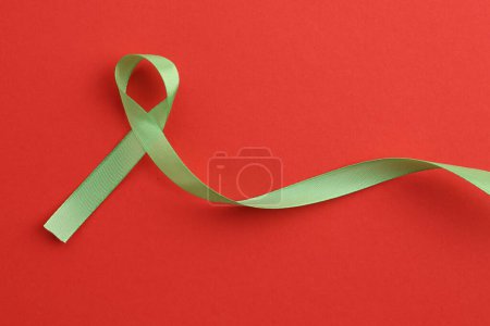 Light green awareness ribbon on red background, top view