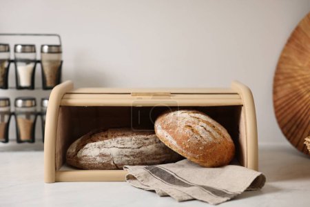 Brotkorb aus Holz mit frisch gebackenen Broten auf weißem Marmortisch in der Küche