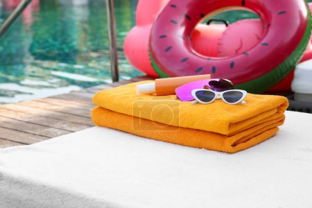 Photo for Beach towels, sunglasses and sunscreen on sunbed near outdoor swimming pool. Luxury resort - Royalty Free Image