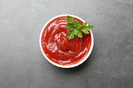 Photo for Delicious tomato ketchup and parsley in bowl on grey textured table, top view - Royalty Free Image