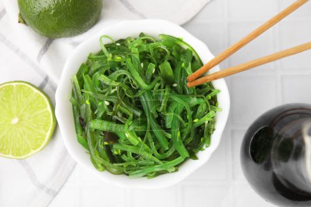 Tasty seaweed salad in bowl served on white tiled table, flat lay