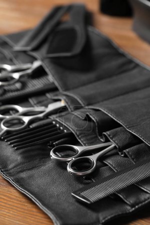 Hairdresser tools. Professional scissors and combs in leather organizer on wooden table, closeup