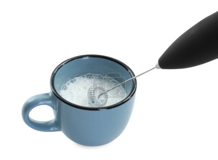 Fouetter le lait dans une tasse avec un mini mélangeur (mousseur) isolé sur blanc, gros plan