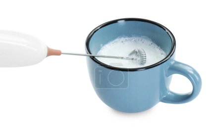 Fouetter le lait dans une tasse avec un mini mélangeur (mousseur) isolé sur blanc, gros plan