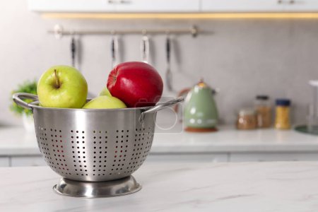 Colander with fresh apples on white marble table in kitchen. Space for text