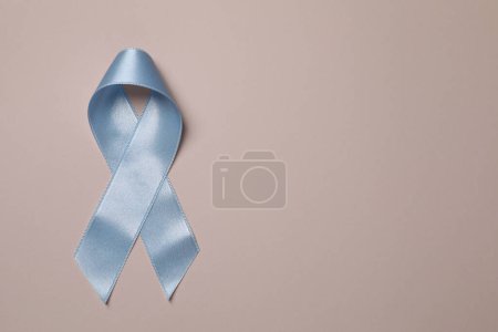 Día Internacional de la Psoriasis. Cinta azul claro como símbolo de apoyo sobre fondo beige, vista superior. Espacio para texto
