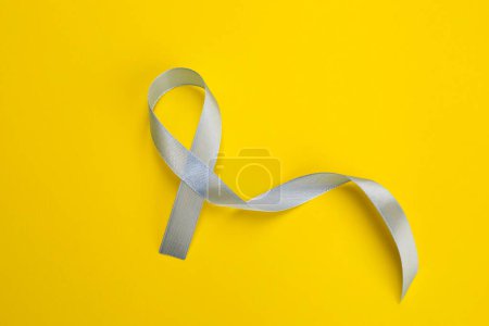 Internationaler Tag der Schuppenflechte. Schleife als Symbol der Unterstützung auf gelbem Hintergrund, Ansicht von oben