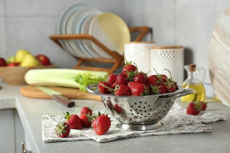 Metal colander with fresh strawberries on grey countertop in kitchen