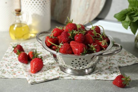 Metal colander with fresh strawberries on grey countertop in kitchen