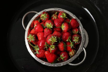 Metal colander with fresh wet strawberries in sink, top view