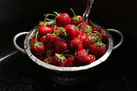 Lavado de fresas frescas bajo agua del grifo en colador de metal en fregadero