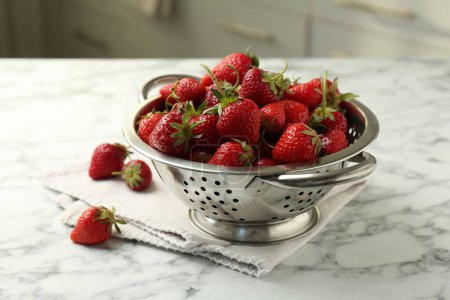 Metal colander with fresh strawberries on white marble table indoors