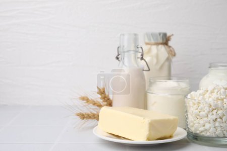 Different dairy products and spikes on white table, space for text