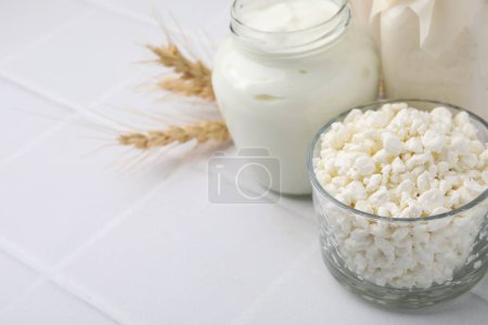 Different dairy products and spikes on white tiled table, space for text