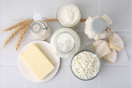 Different dairy products and spikes on white tiled table, flat lay