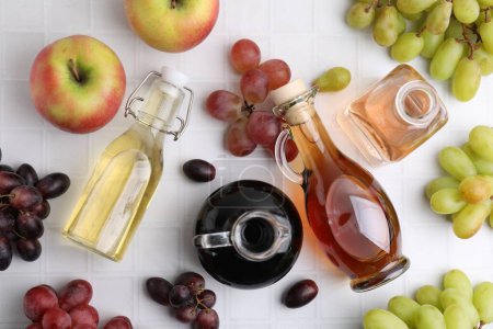 Different types of vinegar and ingredients on light tiled table, flat lay