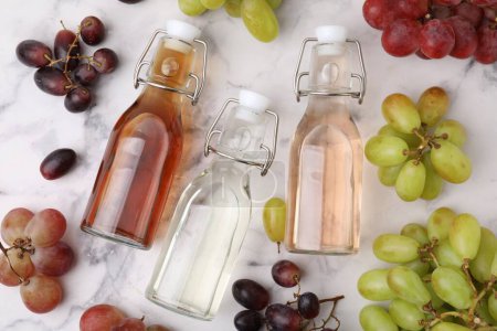 Verschiedene Essigsorten in Flaschen und Trauben auf hellem Marmortisch, flach gelegt