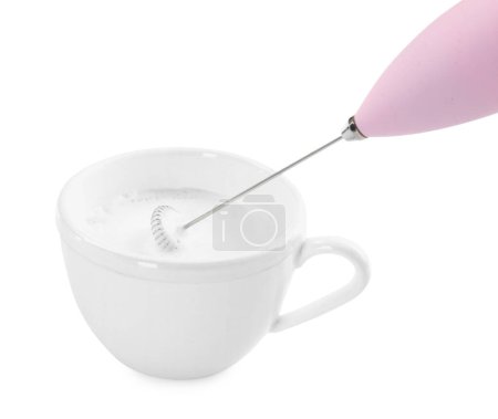 Batiendo la leche en taza con la mini batidora (varita de espuma) aislada en blanco