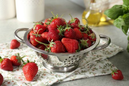 Metal colander with fresh strawberries on grey table