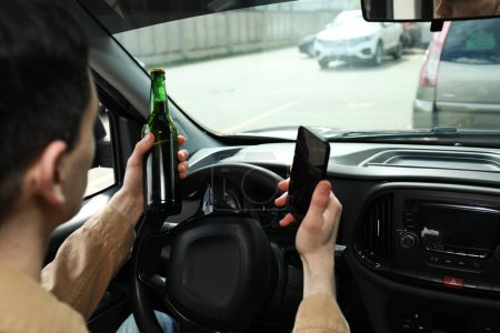 Man with bottle of beer and smartphone in car, closeup. Don't drink and drive concept