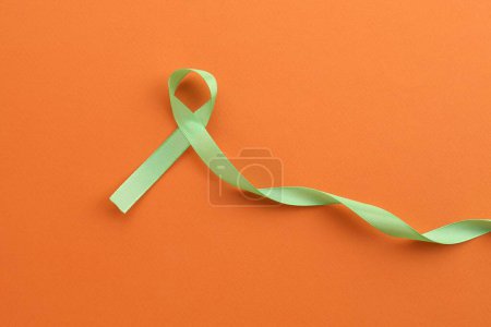 Light green awareness ribbon on orange background, top view