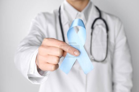 International Psoriasis Day. Doctor with light blue ribbon as symbol of support on white background, closeup