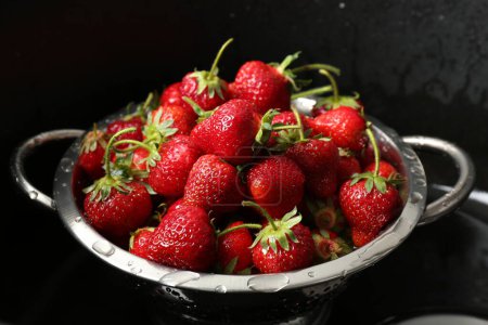 Metal colander with fresh wet strawberries in sink, closeup